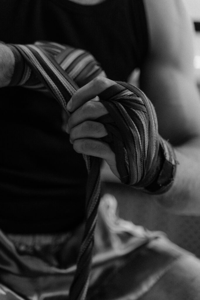 Grayscale photo of an athlete wrapping hands, focusing on wrapped fingers and forearm.